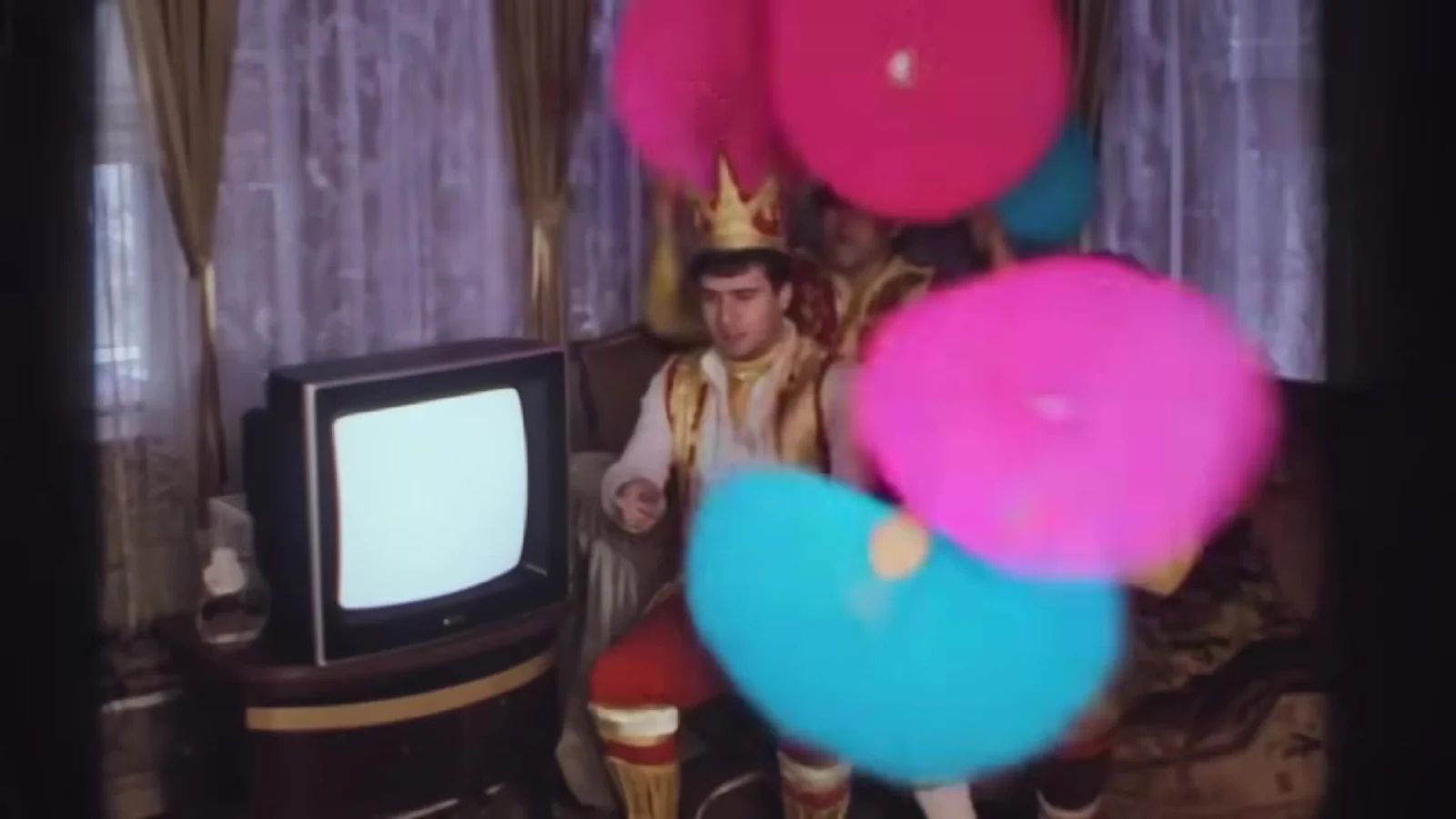 Fotograma del videoclip de «Discutiendo con la IA»: abanicos de plumas rosas y celestes ocupan un salón antiguo con un televisor de tubo encendido