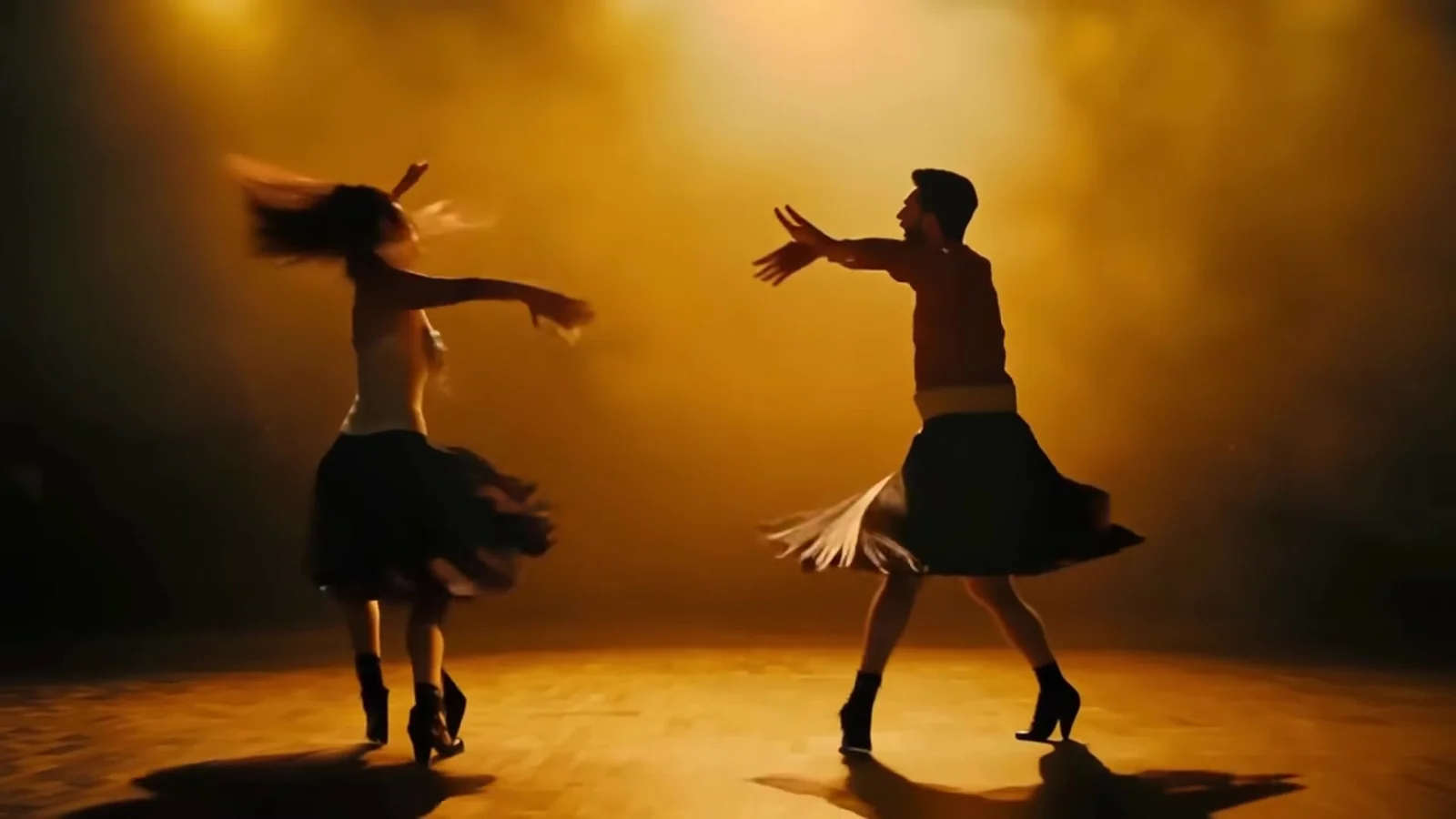 Fotograma del videoclip de «Carta de recomendación»: dos figuras a contraluz saltan y giran con faldas cortas sobre una tarima bañada en luz dorada
