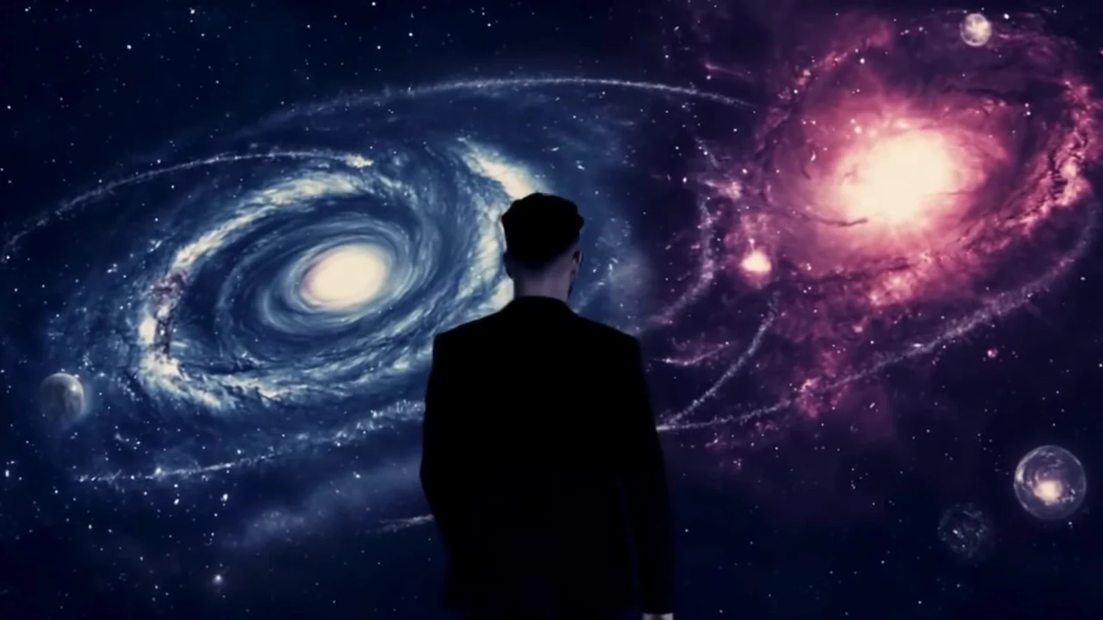 Fotograma del videoclip de «Punto muerto»: la silueta de un hombre, de espaldas, frente a una galaxia en espiral azul y una nebulosa rosa, ya sin muros