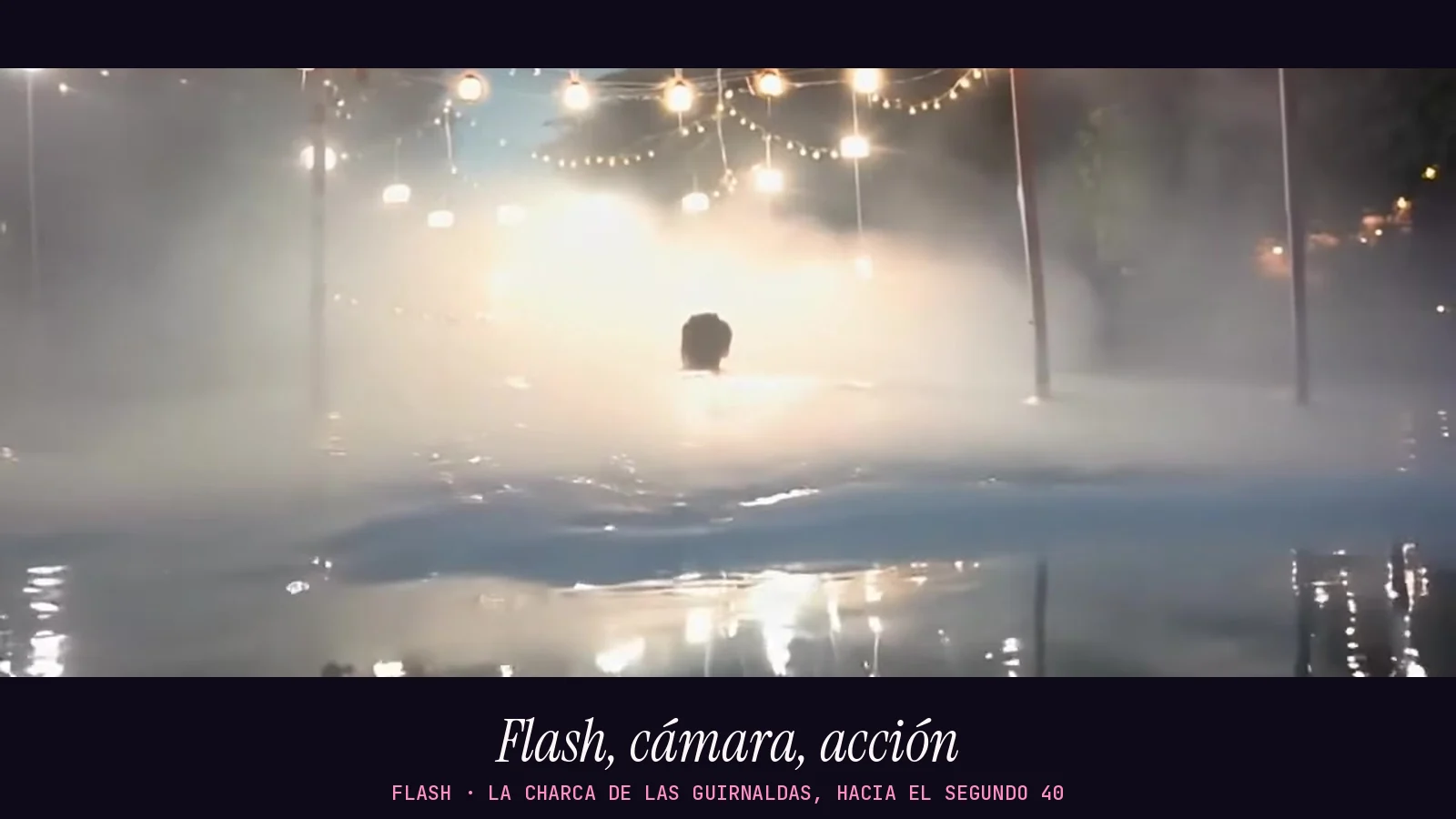 Fotograma panorámico del videoclip de «Flash»: una charca de noche entre niebla bajo una guirnalda de bombillas, con una figura diminuta de espaldas metida en el agua y el renglón «Flash, cámara, acción» debajo