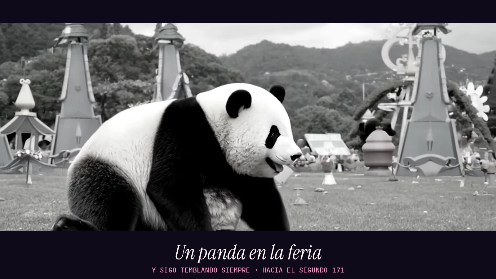 Fotograma panorámico en blanco y negro del videoclip de «Y sigo temblando siempre»: un panda enorme camina por una feria de atracciones con torres puntiagudas y montañas al fondo
