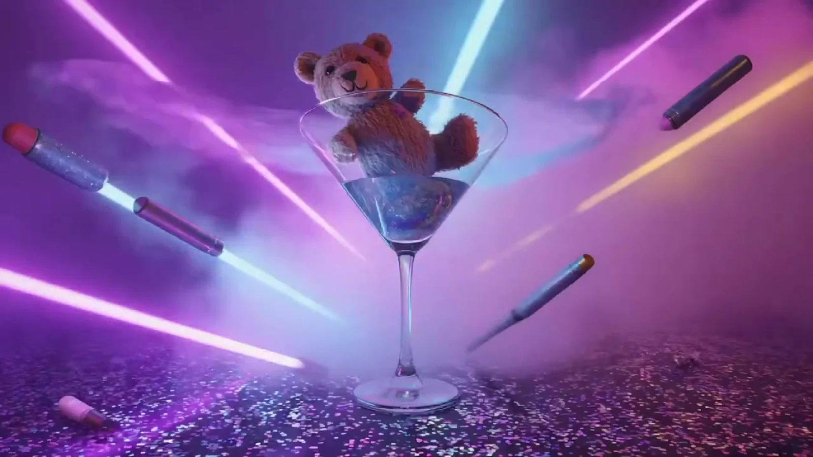 Fotograma del videoclip de «Veneno»: un oso de peluche asomado a una copa de martini gigante entre láseres rosas, pintalabios voladores y purpurina