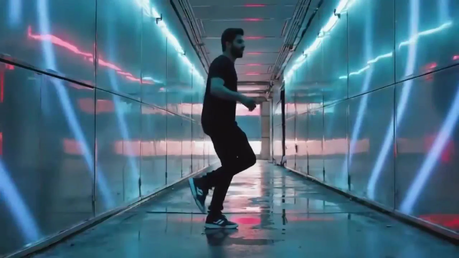 Fotograma del videoclip de «Hipnótico robótico»: un hombre vestido de negro baila en un pasillo largo con líneas de neón rosa y azul y el suelo brillante