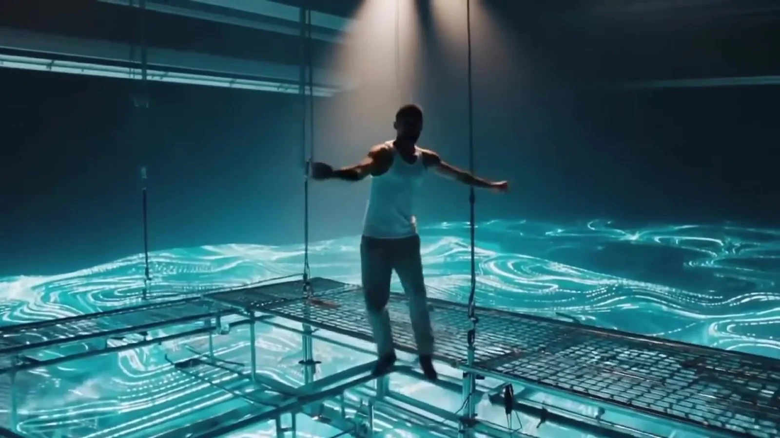 Fotograma del videoclip de «Hipnótico robótico»: un hombre de espaldas con los brazos abiertos sobre un suelo de cristal con agua turquesa luminosa debajo