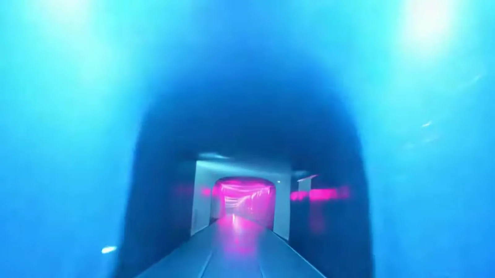 Fotograma del videoclip de «Ya no te quiero»: un túnel de paredes azules redondeadas con una pasarela clara que lleva a un marco iluminado de rosa al fondo