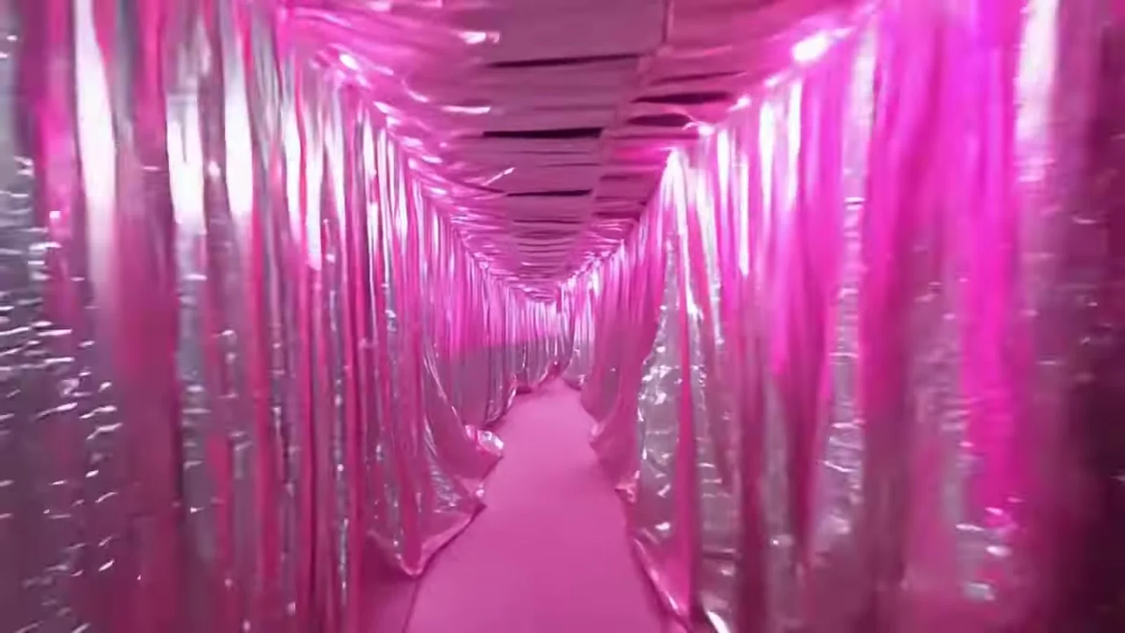 Fotograma del videoclip de «Ya no te quiero»: una galería estrecha con paredes y techo forrados de tela plateada arrugada que brilla con reflejos rosas