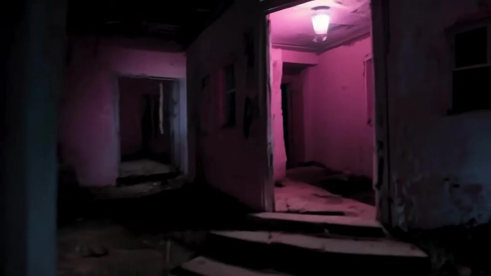 Fotograma del videoclip de «¡Vaya director!»: un pasillo de una casa en ruinas con paredes rotas, escalones de piedra cubiertos de polvo y una lámpara encendida en el techo
