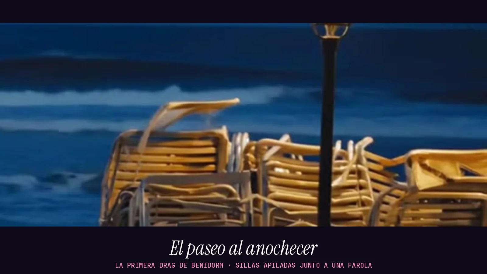 Fotograma panorámico del videoclip de «La primera drag de Benidorm»: sillas de terraza apiladas junto a una farola en un paseo marítimo al anochecer, con el mar azul oscuro al fondo y sin personas