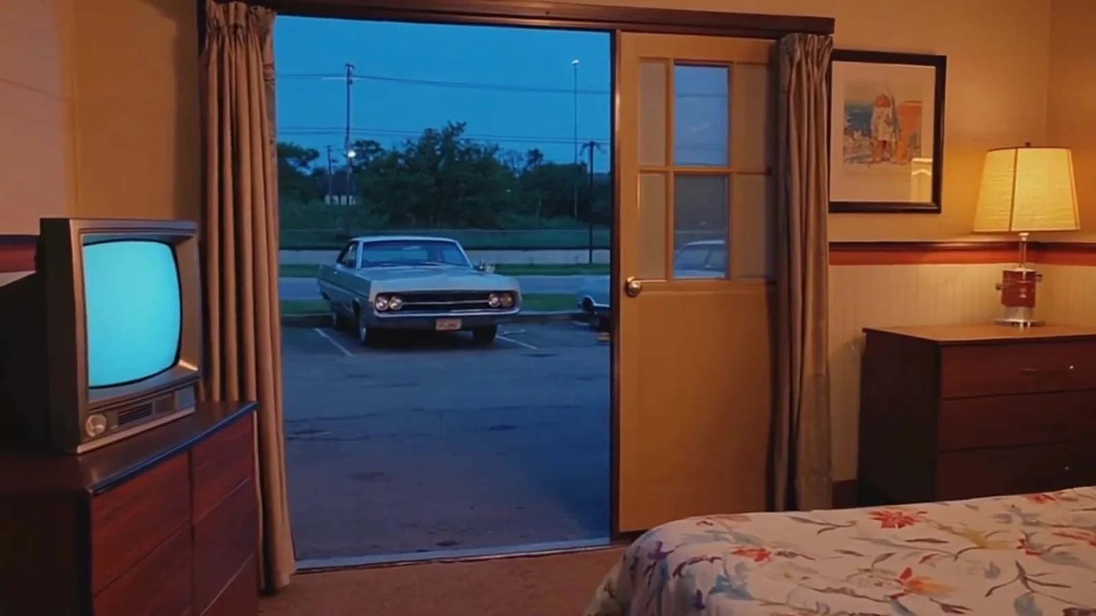 Fotograma del videoclip de «No me gusta el fútbol»: una habitación de motel vacía con un televisor antiguo encendido y la puerta abierta a un aparcamiento con un coche antiguo al anochecer
