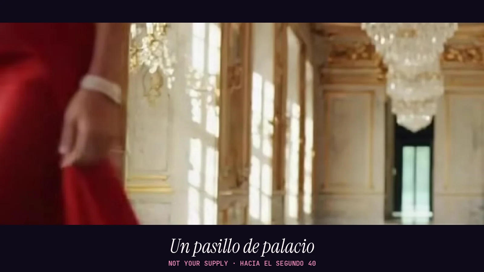 Fotograma panorámico de un pasillo de palacio con mármol, ventanales y lámparas de araña, con el borde de un vestido rojo en primer plano, en el videoclip de «Not Your Supply»