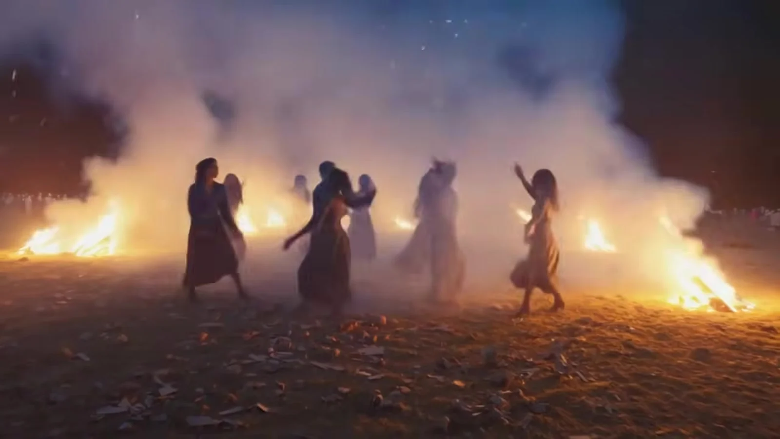 Fotograma del videoclip de «Beat My Post-Traumatic Stress»: siluetas negras a contraluz bailan en un campo de rastrojos entre hogueras y humo blanco