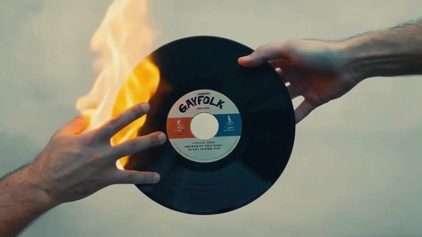 Fotograma del videoclip de «La Boca»: dos manos sostienen un disco de vinilo con la etiqueta GAYFOLK mientras una llama naranja lo quema por un lado