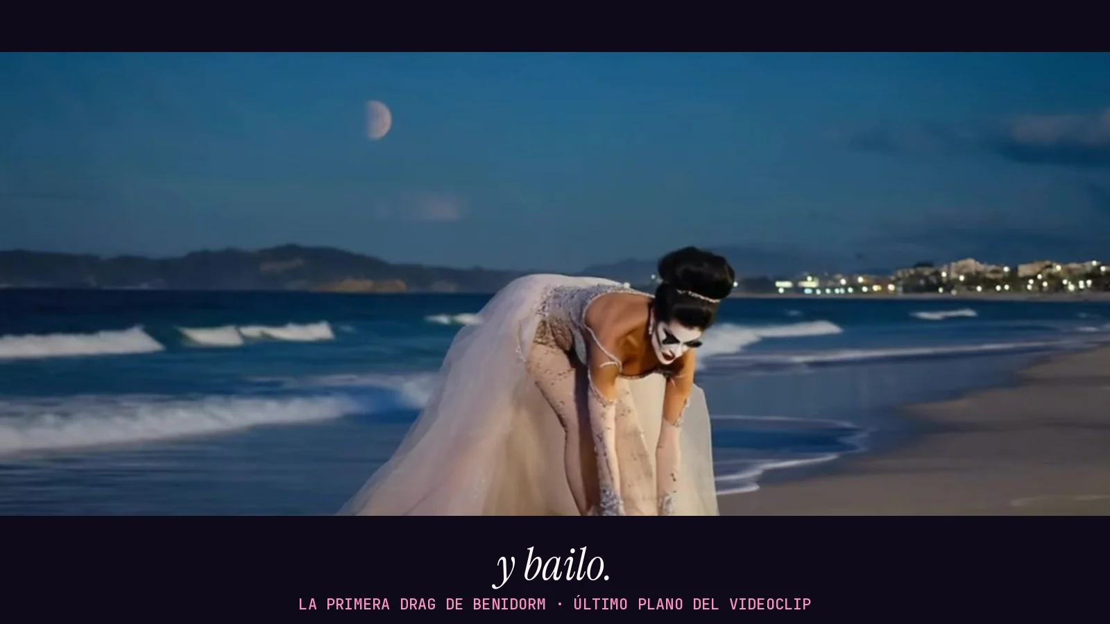 Último plano del videoclip de «La primera drag de Benidorm» en formato panorámico: una reina con vestido blanco de tul se agacha en la orilla bajo la media luna para coger su zapato, con el rótulo «y bailo.» debajo