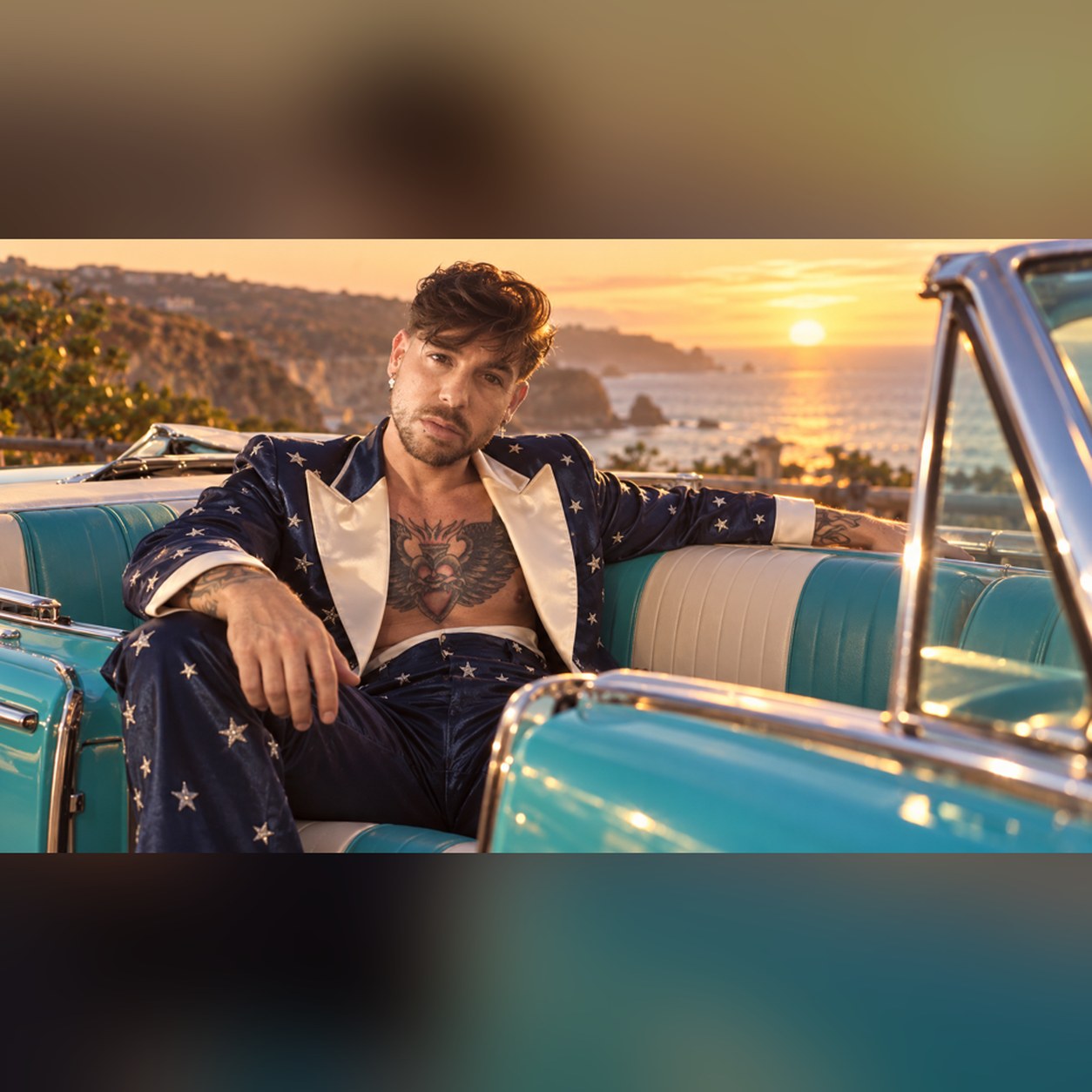 Mike Sain't Louis con traje azul marino de estrellas recostado en un descapotable turquesa frente a la costa al atardecer