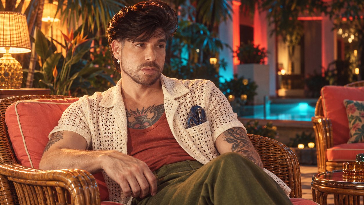 Mike Sain't Louis con chaqueta de punto calado crema y camiseta teja en un sillón de mimbre de noche (serie 100 fotos retro, n.º 088, en color)